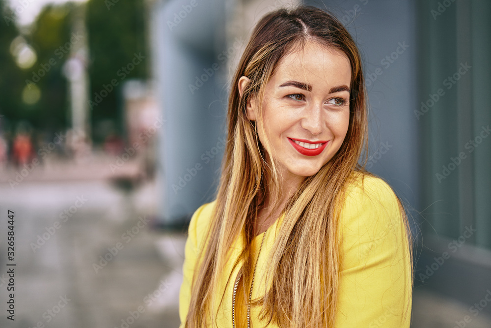 Portrait of a young beautiful laughing woman with long hair and a yellow jacket against the background on a cloudy day. Close-up. Portrait of a young beautiful laughing woman with long hair and a yellow jacket against the background on a cloudy day. Close-up.