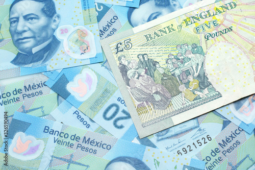 A close up image of a multicolored five pound note from the United Kingdom on a background of Mexican twenty peso bank notes in macro