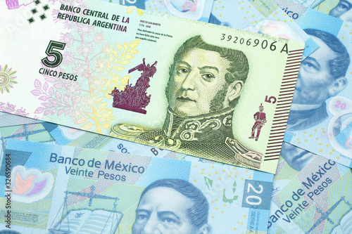 A five peso bank note from Argentina on a background of Mexican twenty peso bank notes close up