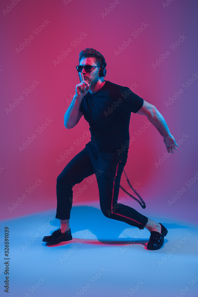 Young caucasian musician in headphones singing on gradient pink-purple background in neon light. Concept of music, hobby, festival. Joyful party host, DJ, stand upper. Colorful portrait of artist.