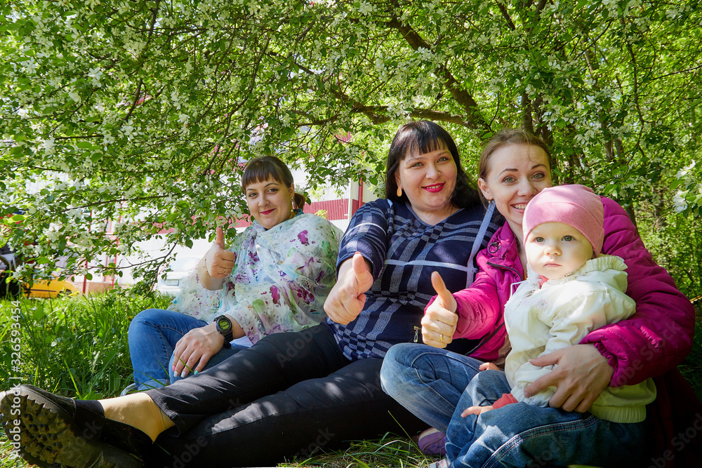 Fototapeta premium Three different funny women and one small seriously girl in the park full of apple blossom trees in a spring day. Aunts and niece in nature landscape