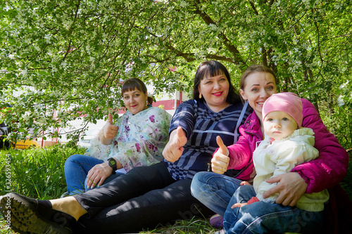 Three different funny women and one small seriously girl in the park full of apple blossom trees in a spring day. Aunts and niece in nature landscape © keleny