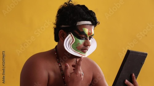 Kathakali dancer checking the shape of chutty in the mirror.  photo