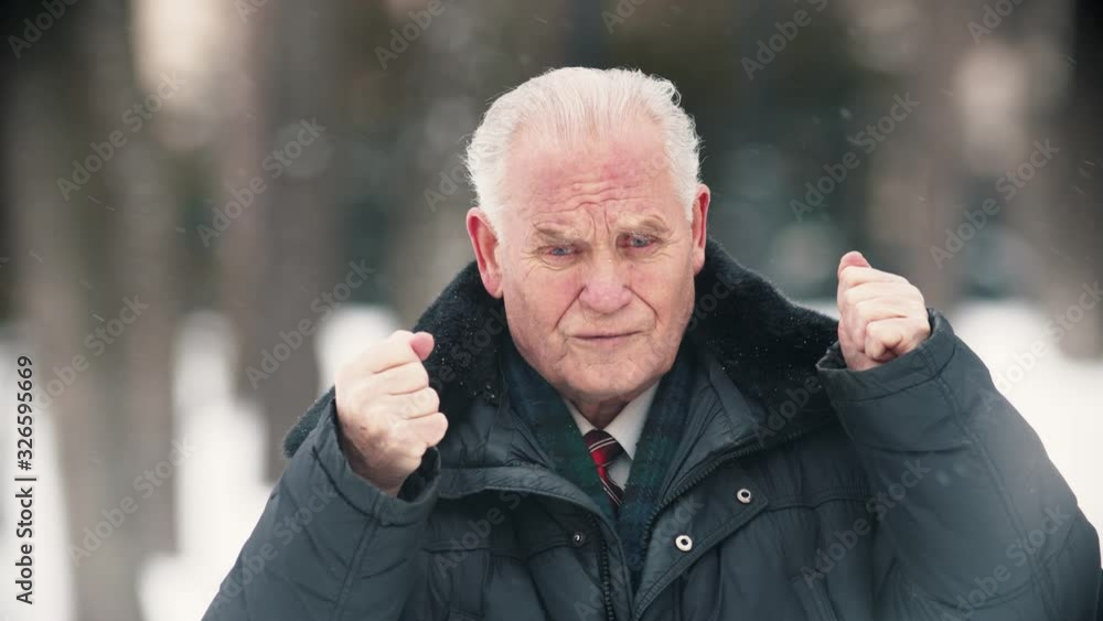 An old man standing outdoors while snowfall - putting his hands up An old man standing outdoors while snowfall - putting his hands up