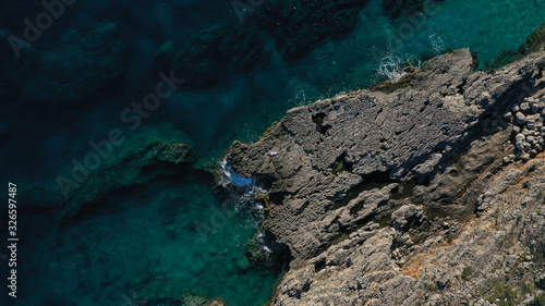 Aerial top down view of beautiful young woman in long white dress lying on rocky coast with cracks in rocky surface. Azure Adriatic sea, foaming waves. Kotor bay, Lustica peninsula, Montenegro. 