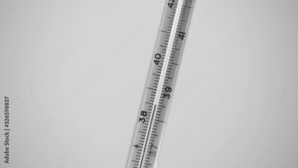 Closeup view black and white video of glass thermometer with raising line of high human body temperature isolated on light grey background. Closeup view black and white video of glass thermometer with raising line of high human body temperature isolated on light grey background.