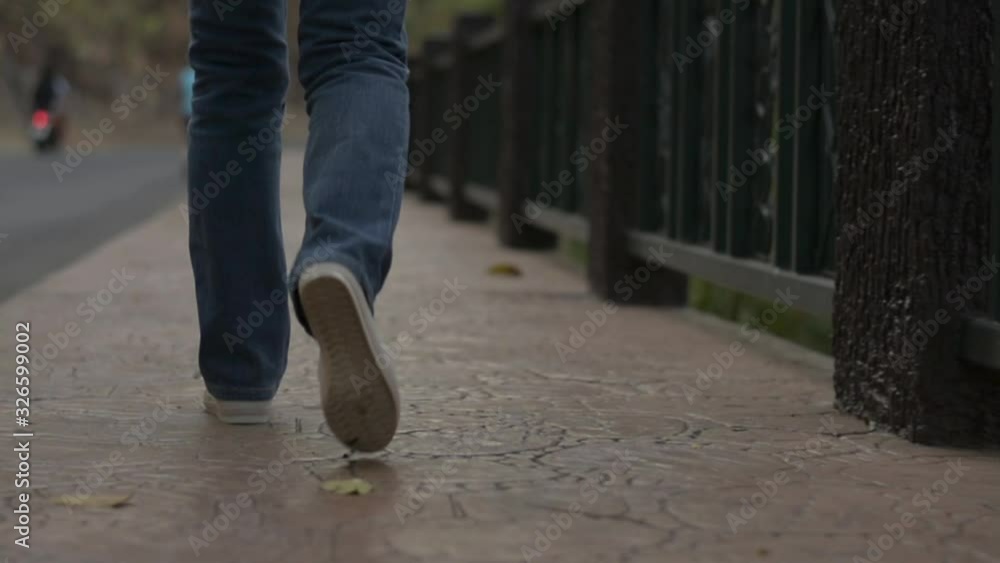 View from rear side of asian woman legs wearing jeans walking leisurely on the footpath along the road in the evening. Close up follow shot with low angle view. Slow motion. View from rear side of asian woman legs wearing jeans walking leisurely on the footpath along the road in the evening. Close up follow shot with low angle view. Slow motion.