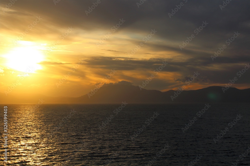 evocative image of sunset over the sea with headland silhouette in the background evocative image of sunset over the sea with headland silhouette in the background