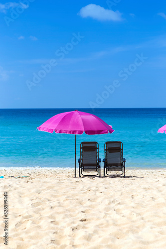 Pink beach umbrella and chairs on beautiful beach with clear blue sky  summer outdoor day light  relaxing on summer break  holiday season