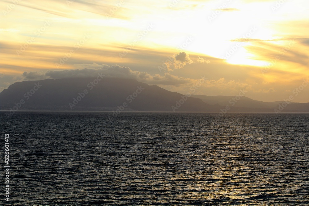 Naklejka premium evocative image of sunset over the sea with headland silhouette in the background