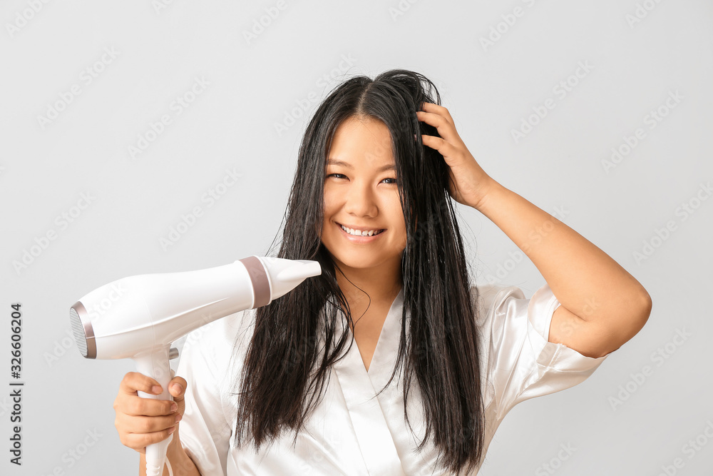 Beautiful Asian woman with hair dryer on light background Beautiful Asian woman with hair dryer on light background