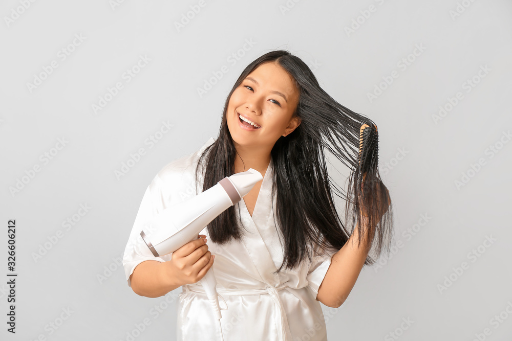 Beautiful Asian woman with hair dryer on light background Beautiful Asian woman with hair dryer on light background