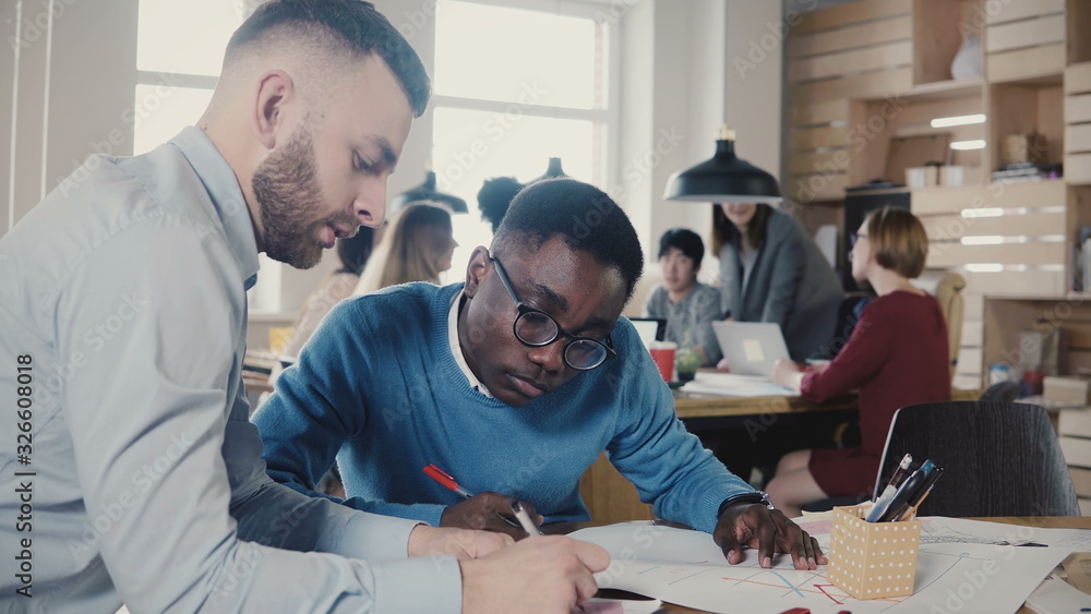 Two multi ethnic colleagues work on architecture project in trendy loft office space, teamwork in the background 4K. Two multi ethnic colleagues work on architecture project in trendy loft office space, teamwork in the background 4K.