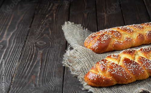 two freshly baked sweet braided bread (challah bread) on a cloth, dark wooden background, close up. copy space for text. photo