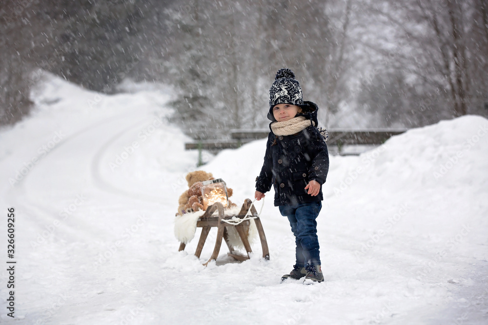 Cute boy playing with teddy bear in the snow, winter time. Little toddler playing with toys on a snowy day