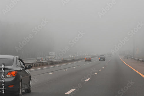 Selective focus. Photo in motion. Cars in the fog on highway. Bad winter weather and dangerous automobile traffic on the road. Vehicles drive in foggy day.