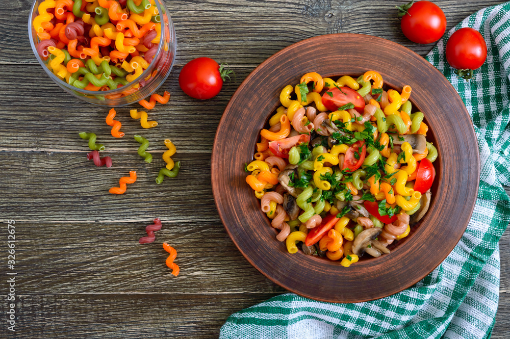 Tasty warm salad. Colored pasta with mushrooms and fresh tomatoes in a bowl on a wooden table. Pasta colorata. The top view Tasty warm salad. Colored pasta with mushrooms and fresh tomatoes in a bowl on a wooden table. Pasta colorata. The top view