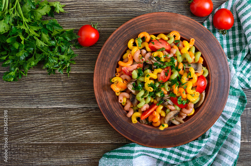 Tasty warm salad. Colored pasta with mushrooms and fresh tomatoes in a bowl on a wooden table. Pasta colorata. The top view
