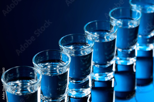 Glasses of vodka on a black reflective background.