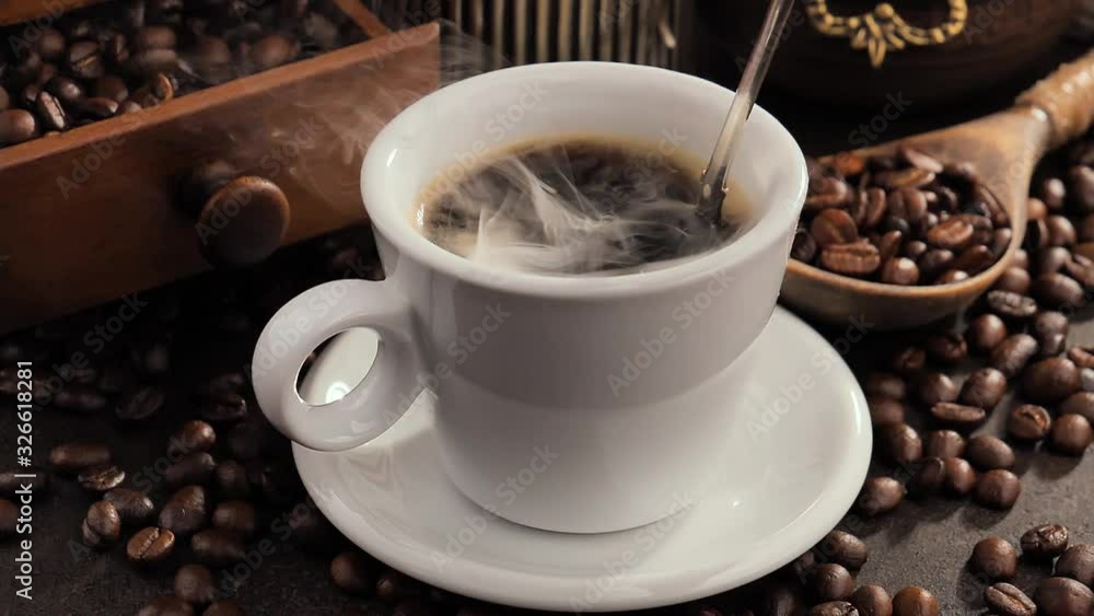 Mixing steaming coffee in a cup with a spoon Mixing steaming coffee in a cup with a spoon