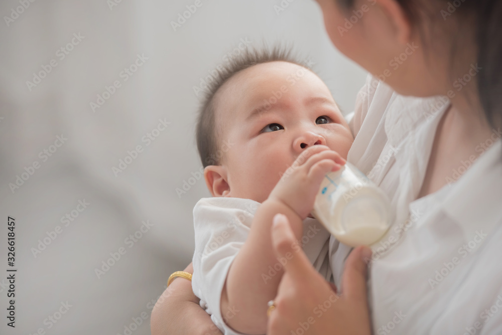 mother holding and feeding baby from milk bottle.portrait of cute baby being fed by her mother using bottle. loving woman giving drink milk to her son. mother feeding newborn baby from bottle at home mother holding and feeding baby from milk bottle.portrait of cute baby being fed by her mother using bottle. loving woman giving drink milk to her son. mother feeding newborn baby from bottle at home