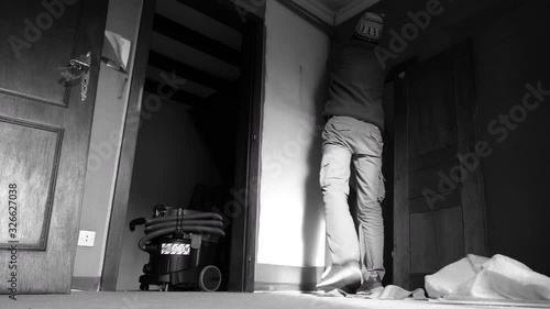 Rear view of young man removing textile isolation cover from the bedroom wall in old house apartment during renovation with industrial vacuum cleaner seen in lower corner of the frame photo