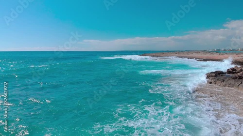 flight over the sea seashore, aerial drone view of waves crashing at rocky cliff with splashing and white foam, view of stones in blue water, cyprus Aya Napa photo