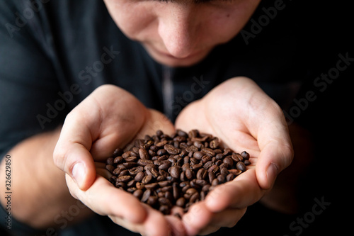 Barista man holds roasted coffee grains in his hands and sniffs them