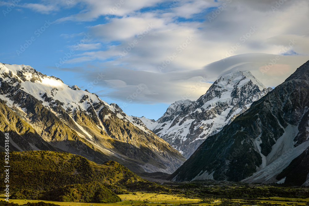 High mountain views on the top of the mountain are white snow in the summer with sky and clouds with green grass throughout the area in Mount Cook National Park in south island of New Zealand