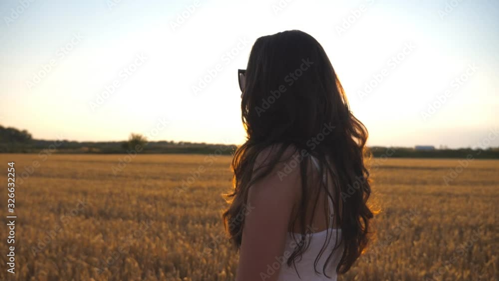 Beautiful girl is walking along wheat field with sun flare at background. Profile of young woman going at the meadow at sunset. Summer leisure at nature concept. Side view Close up Slow motion Beautiful girl is walking along wheat field with sun flare at background. Profile of young woman going at the meadow at sunset. Summer leisure at nature concept. Side view Close up Slow motion