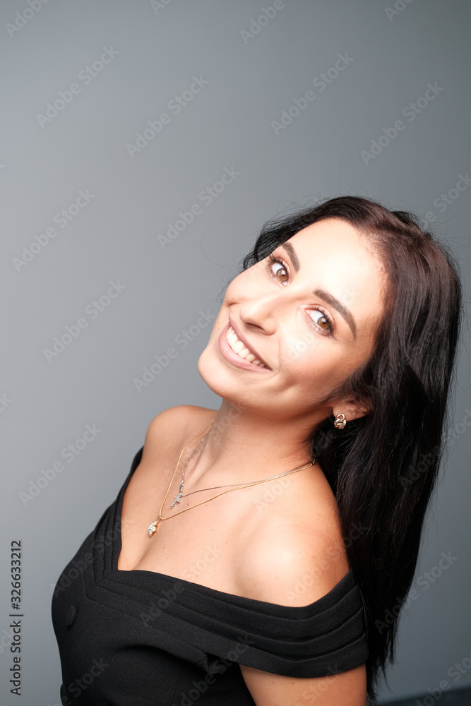 A large portrait of a middle-aged woman (30-35 years old) with dark hair and brown eyes in a black dress on a light background. A large portrait of a middle-aged woman (30-35 years old) with dark hair and brown eyes in a black dress on a light background.