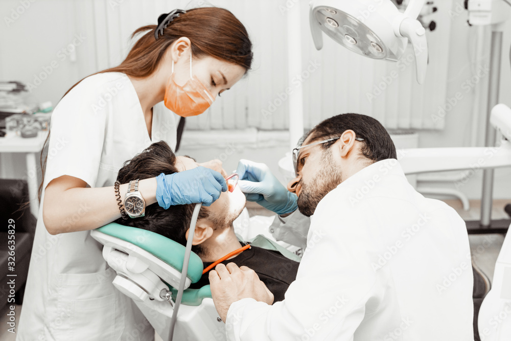 Obraz premium Two dentists treat a patient. Professional uniform and equipment of a dentist. Healthcare Equipping a doctor’s workplace. Dentistry