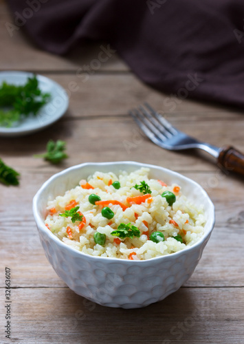 Vegetarian rice dish with vegetables and green peas on a wooden background.