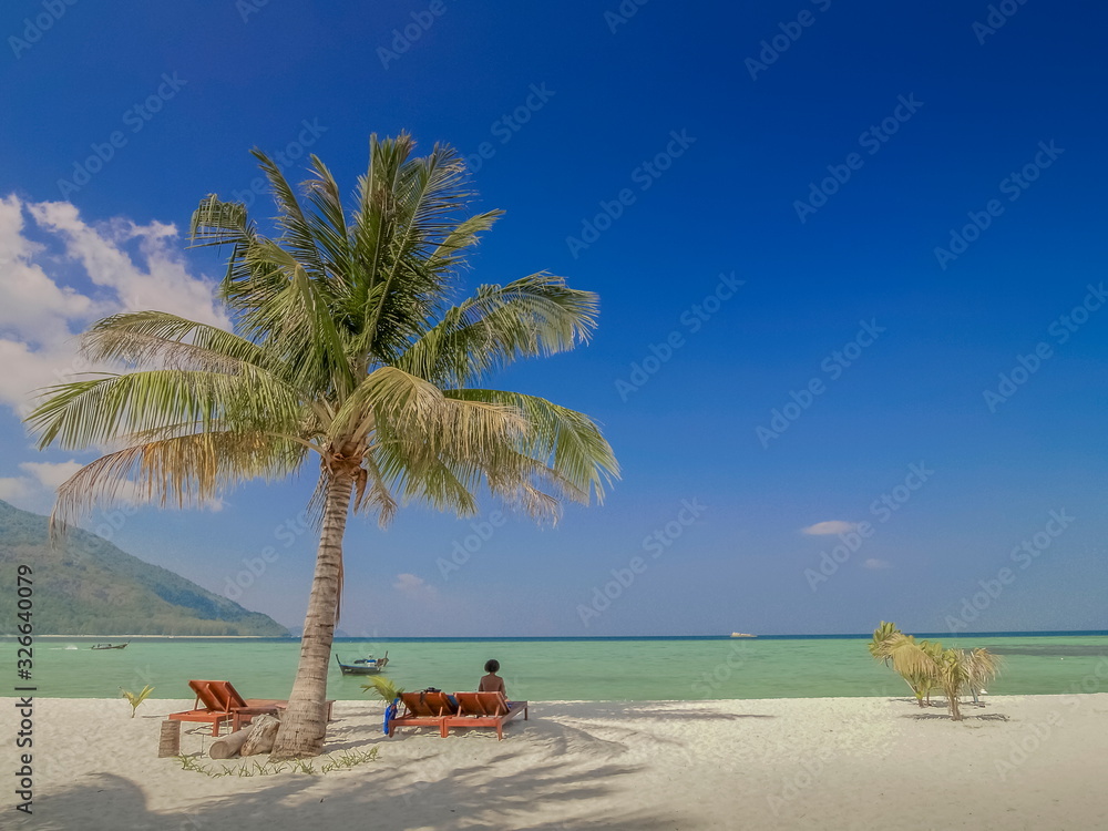 Fototapeta premium view seaside of coconut tree with tourist relax on beach chair and blue-green sea with blue sky background, Lipe island, Satun, southern Thailand.