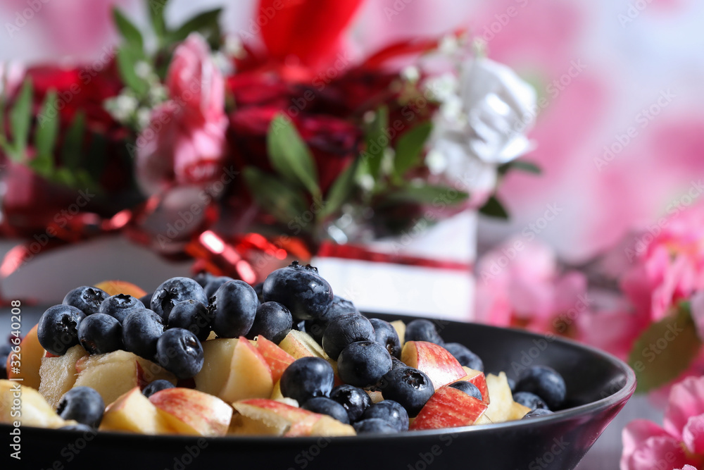 Fruit salad on a dark plate with red roses bouquet on the background Fruit salad on a dark plate with red roses bouquet on the background