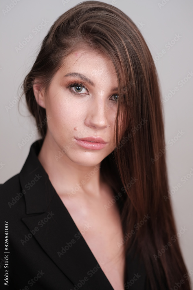 Close-up portrait of a beautiful cute girl with long hair and in a black jacket on a light background. Girl posing for the photographer in a photo studio. Close-up portrait of a beautiful cute girl with long hair and in a black jacket on a light background. Girl posing for the photographer in a photo studio.