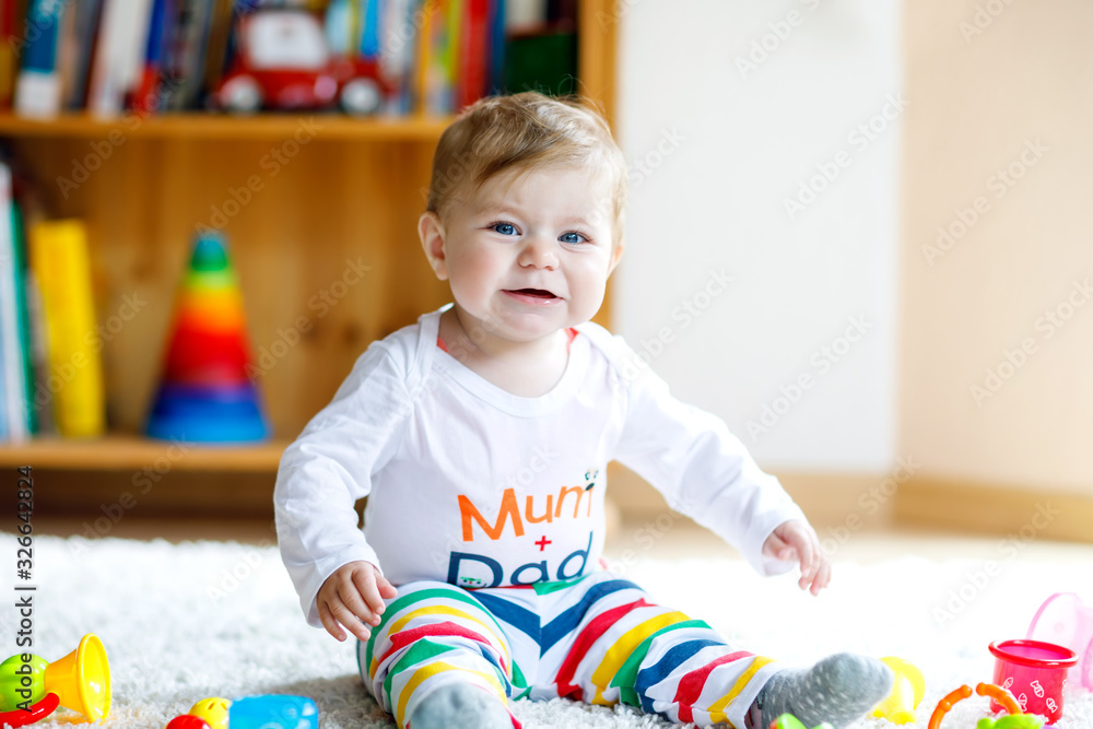 Happy baby girl playing with educational toys in nursery. Happy healthy child having fun with colorful different toys at home. Baby development and first steps, learning to play and to grab. Happy baby girl playing with educational toys in nursery. Happy healthy child having fun with colorful different toys at home. Baby development and first steps, learning to play and to grab.
