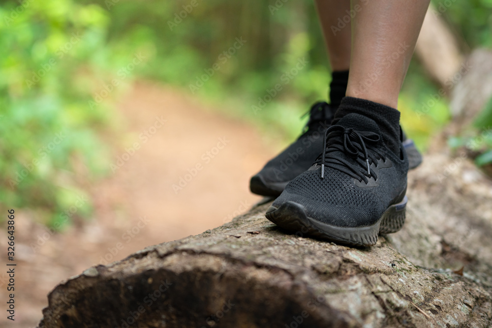Close-up action at trail or trekking runner's foot during standing on timber, it also have pathway in the forest as background. Sport and adventure recreation concept photo.