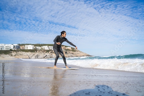 Man on a wetsuit riding a skimboard over wetsand in Cala Mesquida (Mallorca) photo