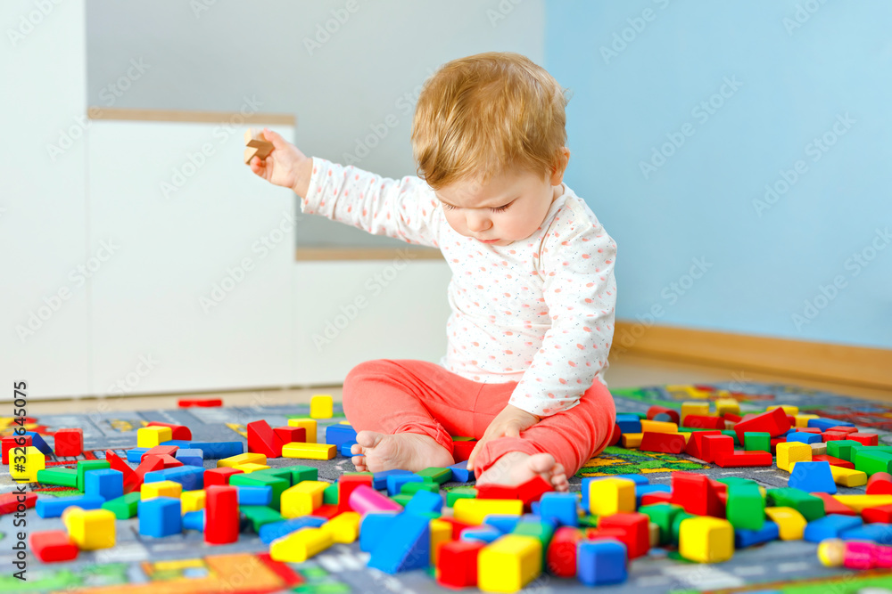 Adorable baby girl playing with educational toys . Happy healthy child having fun with colorful different wooden blocks at home in domestic room. Baby learning colors and forms Adorable baby girl playing with educational toys . Happy healthy child having fun with colorful different wooden blocks at home in domestic room. Baby learning colors and forms