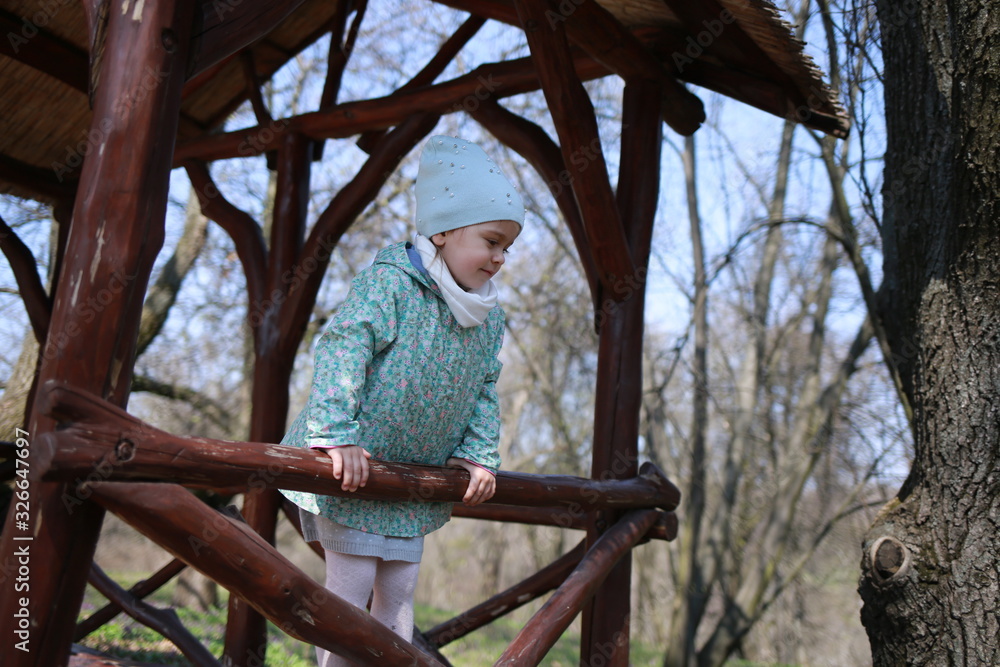 Little girl plays in a wooden gazebo in a spring botanical garden where primroses bloom Little girl plays in a wooden gazebo in a spring botanical garden where primroses bloom