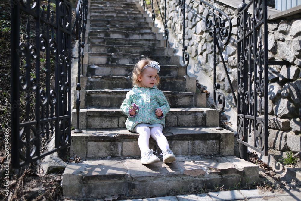  A little girl sits on the steps in the spring botanical garden with an apple in her hands and eats it where the primroses bloomed