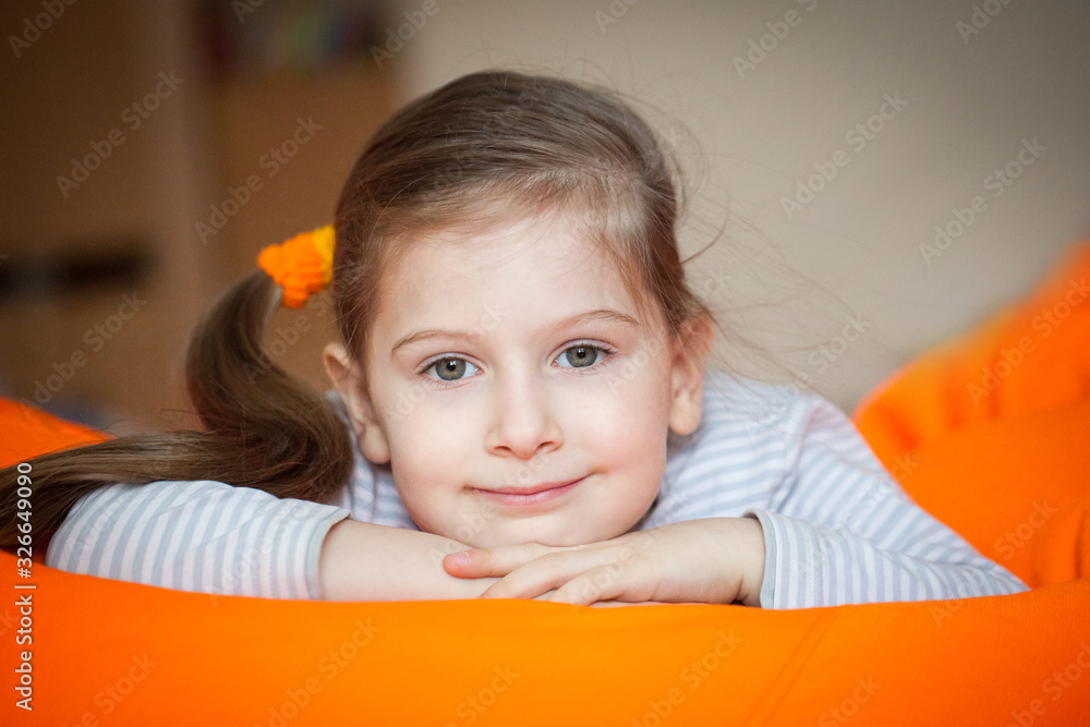 Happy little girl wallows in an orange bean bag chair Happy little girl wallows in an orange bean bag chair