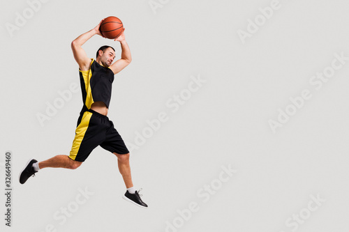 Side view of basketball player posing mid-air while throwing ball with copy space