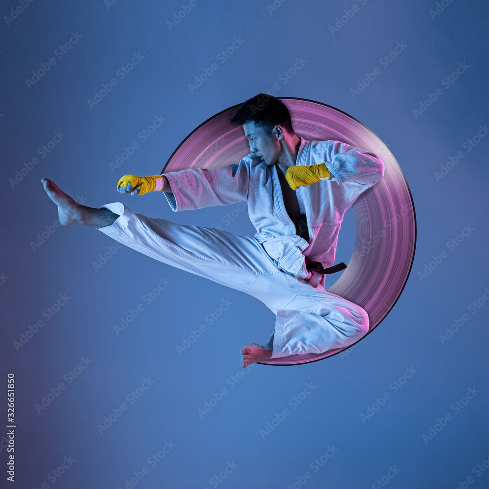 Obraz premium Concept of motion and action in sport. Confident korean man in kimono practicing hand-to-hand combat, martial arts. Blue background, neon light. Sport, healthy lifestyle, movement. Abstract design.