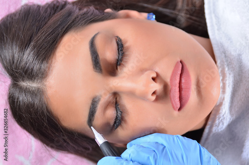 Micro pigmentation or permanent make up on female eyebrow. Beautician applying tattoo with a professional tool in beauty studio. Close up  selective focus and top view