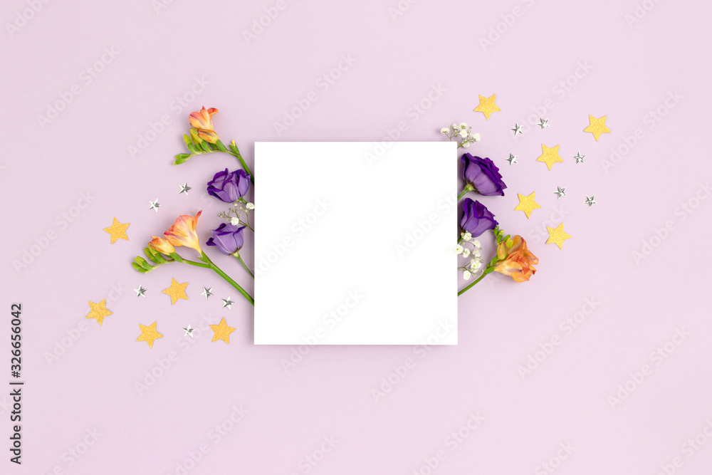 Blank paper card mockup with eustoma, freesia flowers and stars confetti. Festive concept with place for text on a purple pastel background.