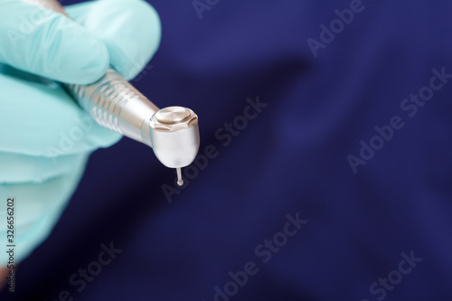 Dentist's hand in green examination glove with dental handpiece.