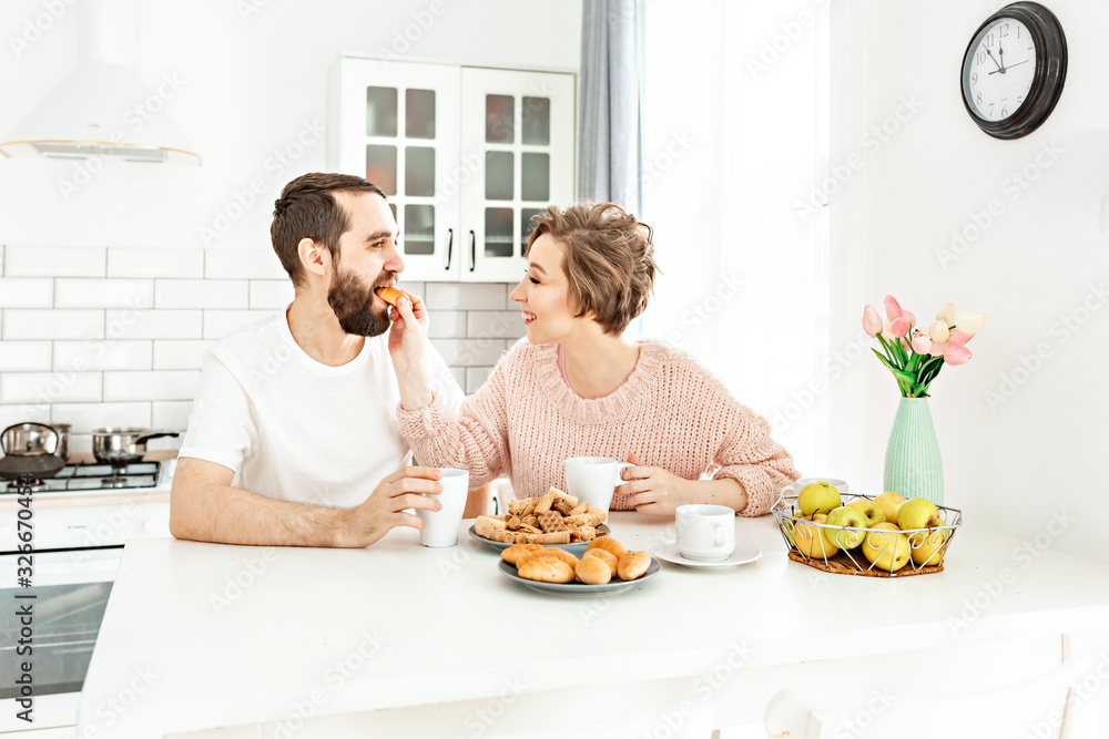 Portrait of a pretty young couple holding  croissant  while standing at the kitchen