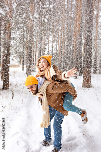 Girl having fun riding on her man in winter forest at the snowfall